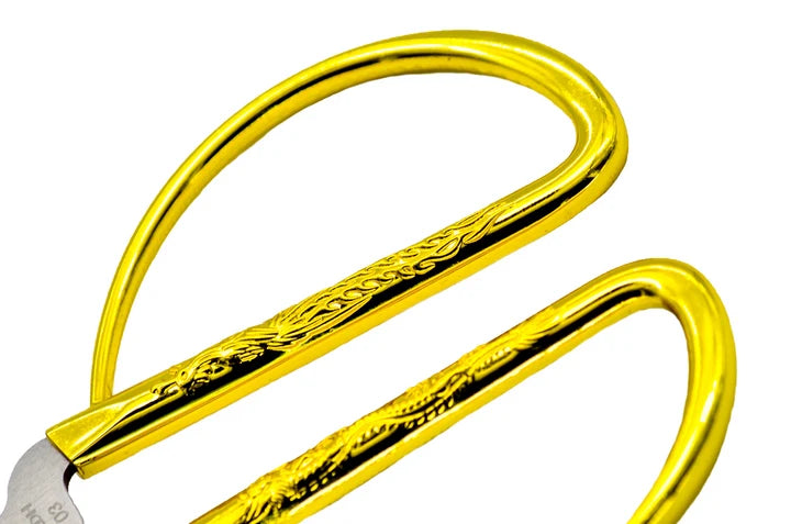 Close-up of a pair of scissors with shiny gold handles and a silver metal blade, shown on a plain white background for sewing and crafting.