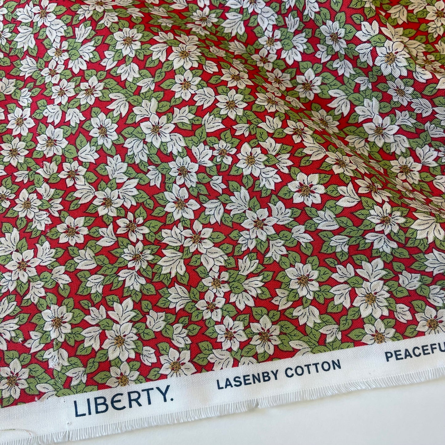 Fabric with white poinsettias on a red background from Liberty Fabrics for Christmas sewing, quilting, and crafting. 