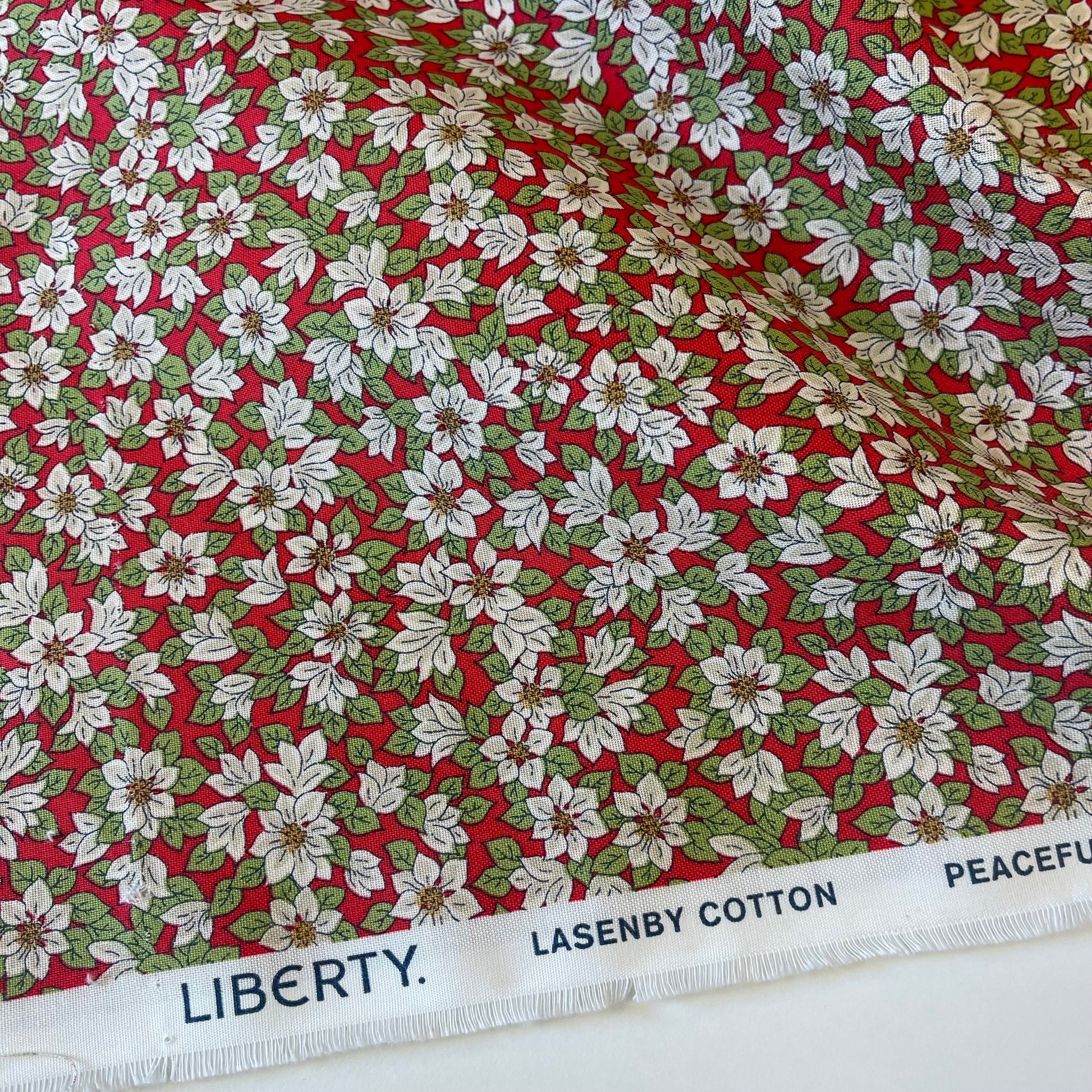 Fabric with white poinsettias on a red background from Liberty Fabrics for Christmas sewing, quilting, and crafting. 