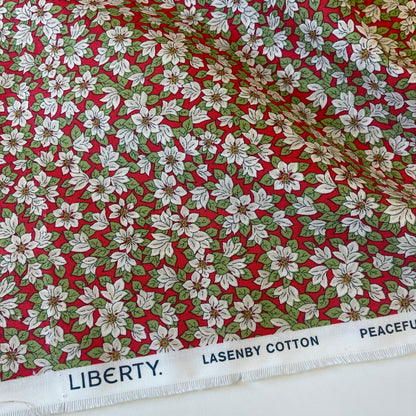 Fabric with white poinsettias on a red background from Liberty Fabrics for Christmas sewing, quilting, and crafting. 