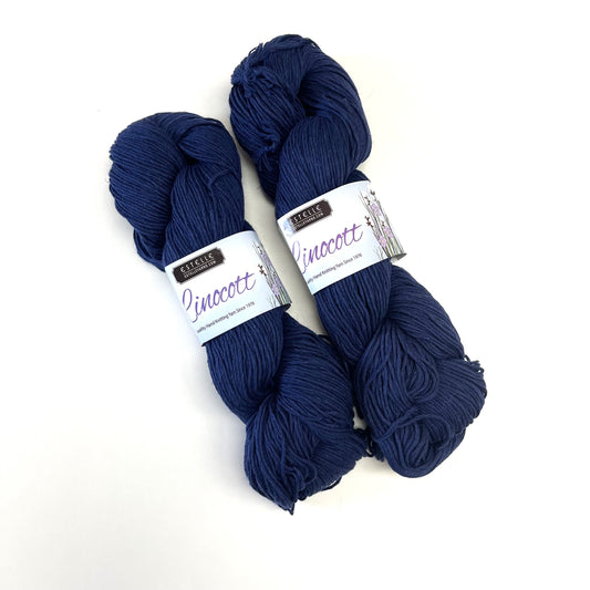 Two skeins of dark navy blue yarn with white paper bands labeled 'Raspberry Creek Fabrics' and 'Pinocott', displayed on a clean white background.