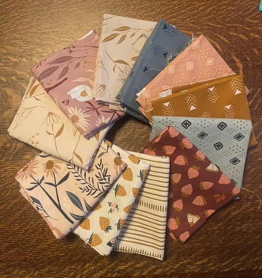 Collection of patterned fabric swatches on a wooden surface. bundle of half yard fabric cuts from figo fabrics. 