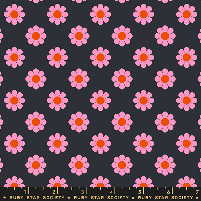 Fabric with a repeating pattern of pink daisies with orange centers on a dark charcoal gray background, with a yellow measuring ruler along the bottom edge showing Ruby Star Society branding.