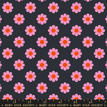Fabric with a repeating pattern of pink daisies with orange centers on a dark charcoal gray background, with a yellow measuring ruler along the bottom edge showing Ruby Star Society branding.