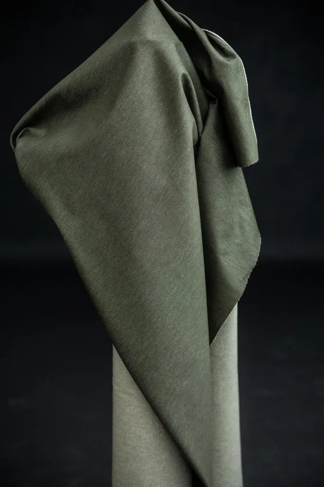 Green denim fabric organic cotton draped over a stand against a dark background
