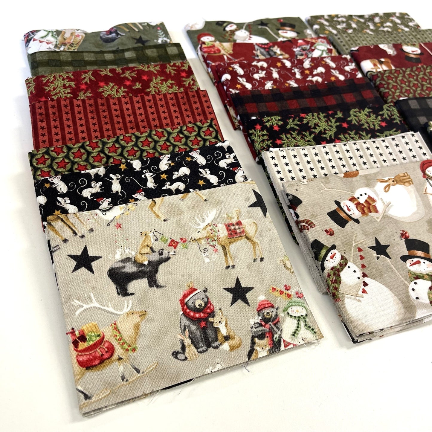 Collection of Christmas-themed fabric swatches with reindeer, snowmen, and other winter elements for sewing and quilting