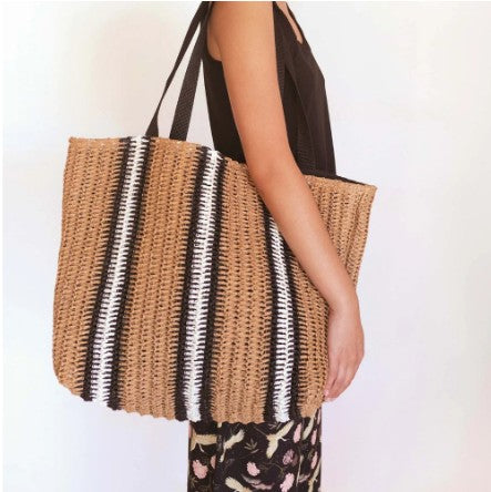 Person holding a woven raffia bag with black and white stripes on a plain background