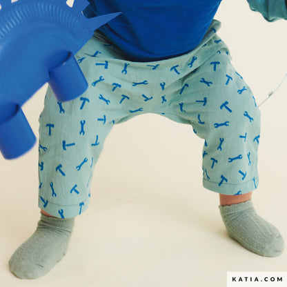 Child wearing light green cotton pants with blue tool pattern and gray socks on a plain background