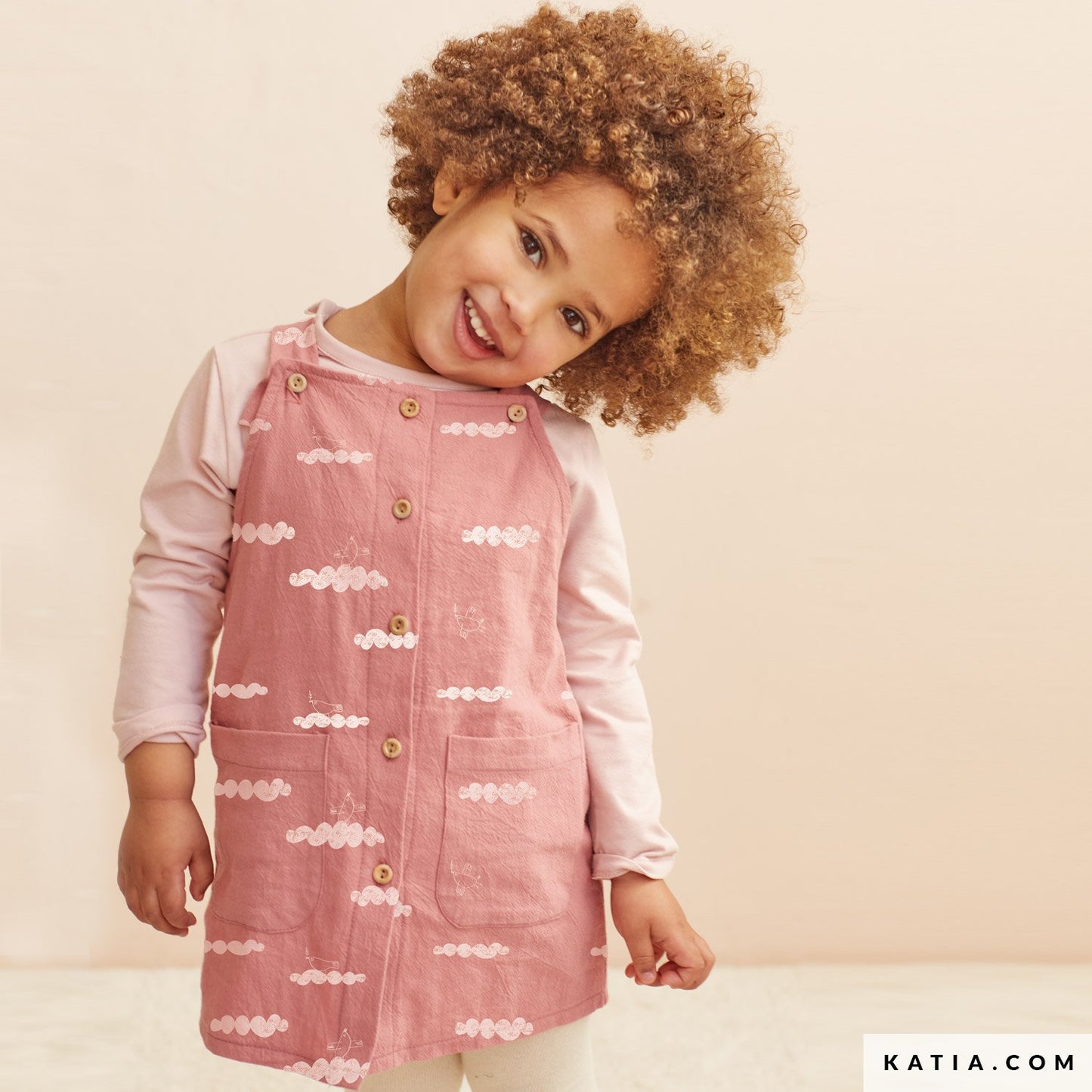 Child wearing a pink dress with cloud pattern on a beige background