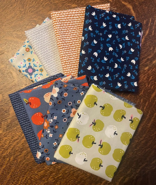 Collection of fabric swatches with various patterns on a wooden surface. half yard bundle from ruby star society