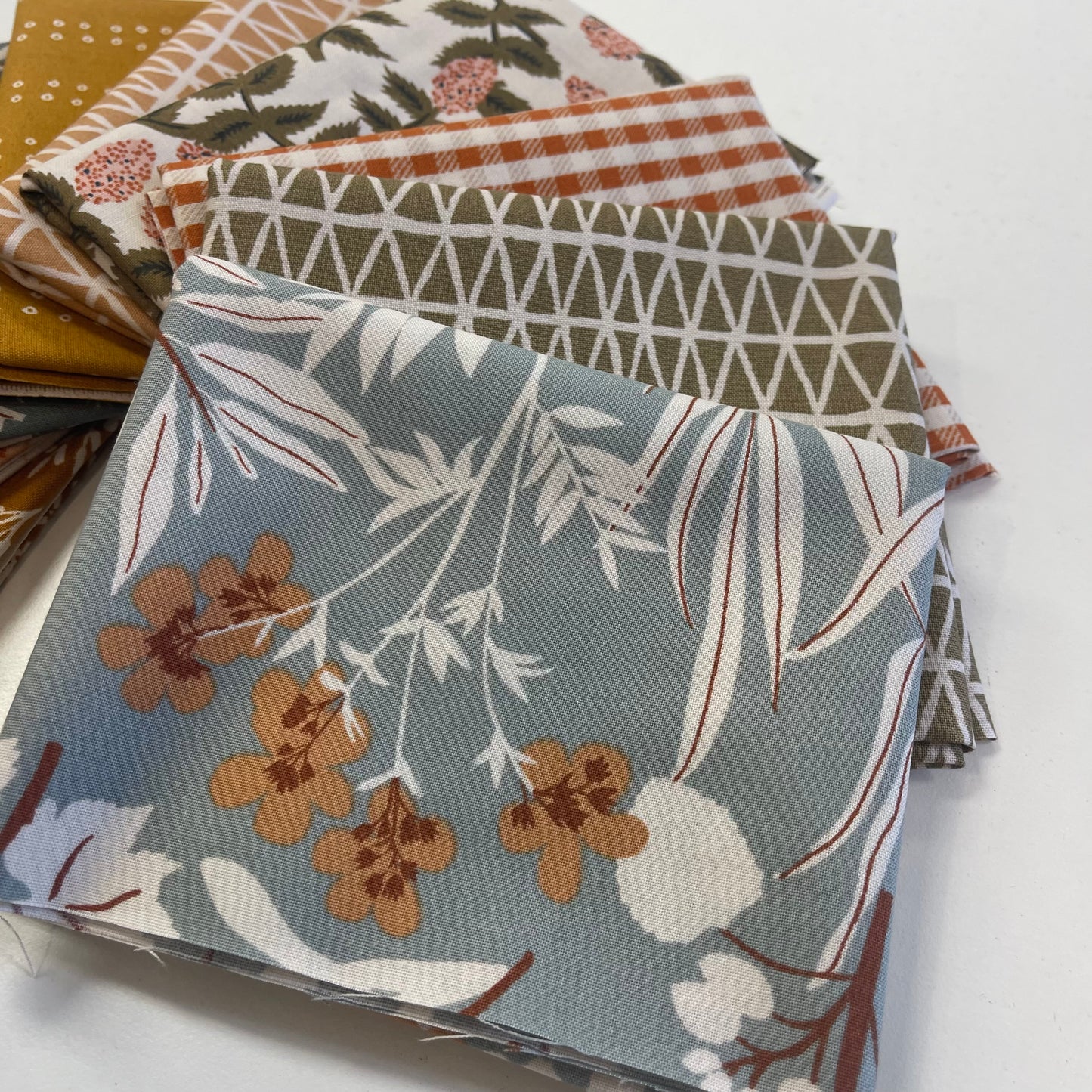 Stack of fabric swatches with various patterns on a white background for quilting and sewing
