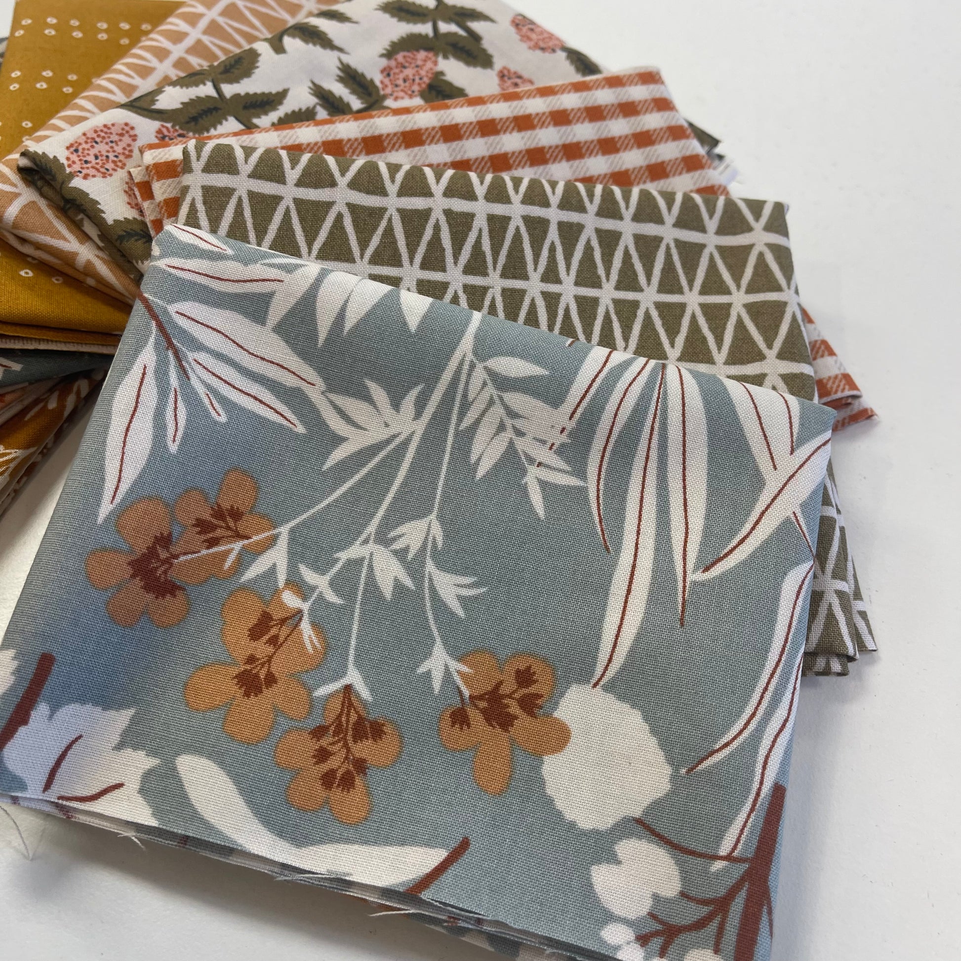 Stack of fabric swatches with various patterns on a white background for quilting and sewing
